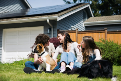 A family plays with their dogs in the front yard of their home after finding the best solar provider to install solar panels